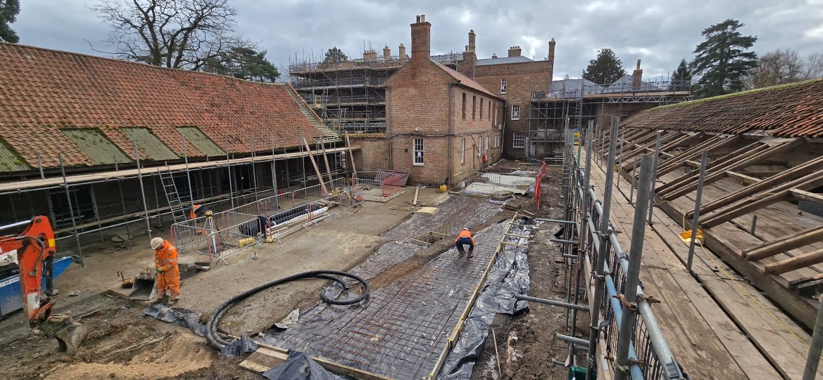Wide view down the stable courtyard, mesh reinforcement laid over DPM ready for pour, with the scaffolded hall behind
