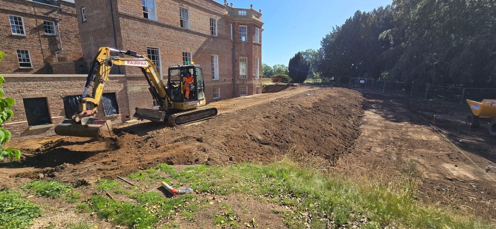 Tracked midi excavator cutting and pushing spoil alongside the hall