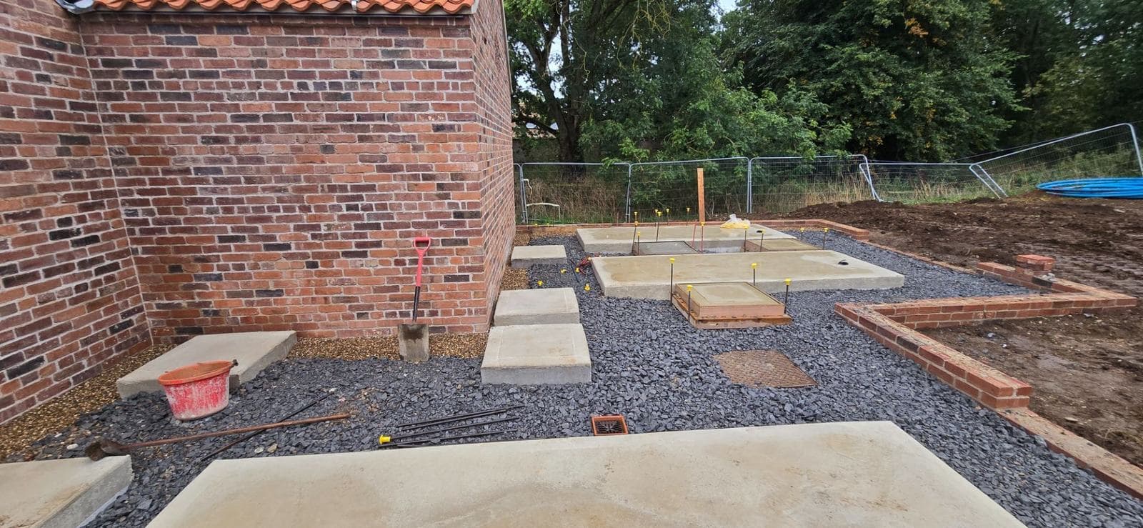Concrete pad foundations with capped starter bars beside a brick barn