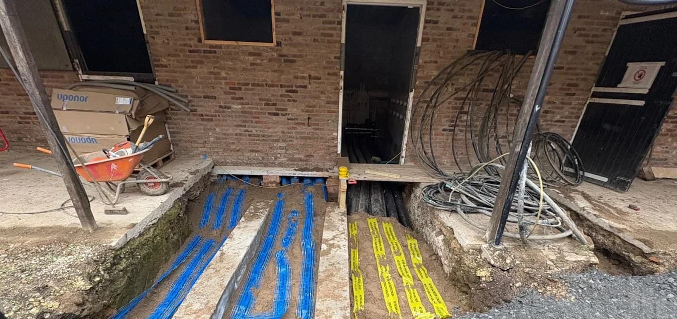 Blue water ducts and black ducts running into the building under blue and yellow marker tape