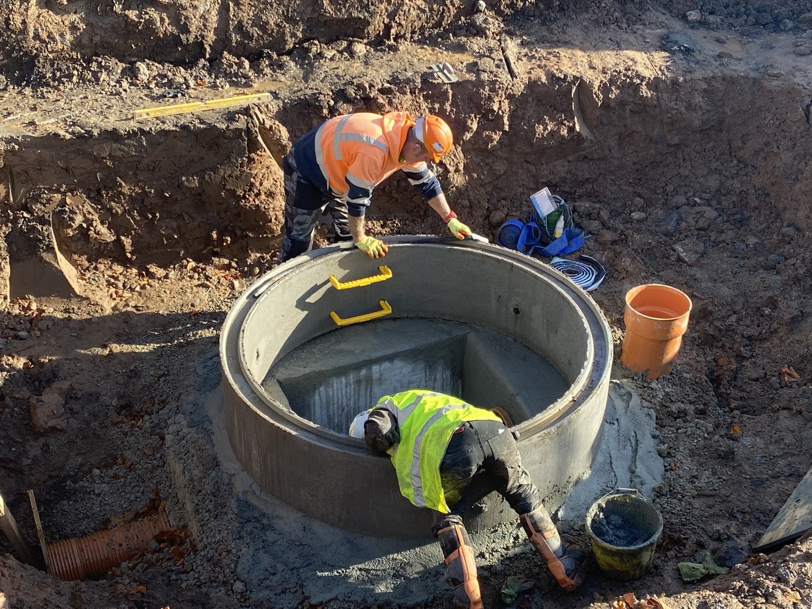 Precast concrete manhole chamber being benched and finished in an open excavation